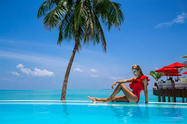 在马尔代夫热带岛屿的游泳池里 穿着红色泳衣的优雅的晒黑的女人 美丽的比基尼女孩在游泳池与地平线上的视野 在美丽的印度洋景观的水池边的性感模特 — 图库照片