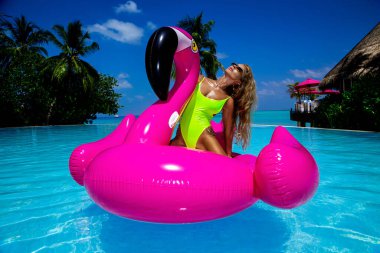 Havuzdaki pembe flamingoda bronzlaşmış güzel bir kadın. Maldivler adasında mayolu çekici bir kız. Maldivler 'deki lüks bir tatil köyünde mükemmel bir vücut bikini modeli. Lüks seyahat. Yaz zamanı..