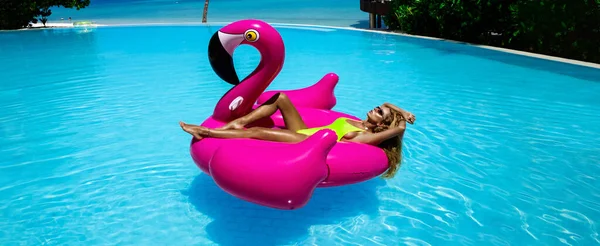 Havuzdaki pembe flamingoda bronzlaşmış güzel bir kadın. Maldivler adasında mayolu çekici bir kız. Maldivler 'deki lüks bir tatil köyünde mükemmel bir vücut bikini modeli. Lüks seyahat. Yaz zamanı..