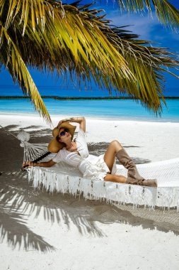 Şık elbiseli zarif bir kadın ve Maldivler adasındaki tropik plajda büyük bir şapka. Yaz modası. Kadın model kumlu sahilde poz veriyor. Maldivler manzarası. Lüks Seyahat.