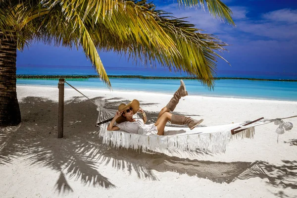 马尔代夫岛上热带海滩上穿着时髦服装头戴大帽子的优雅女人 夏季时尚 女模特正躺在沙滩上 马尔代夫的风景 豪华旅游 — 图库照片