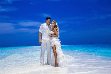 Yaz aşkı. Gelinlik giymiş güzel mutlu genç çift Maldivler 'de bir plajda duruyor. Nişanlar ve düğün Maldivler 'in cennet adasındaki plajda. Lüks seyahat.