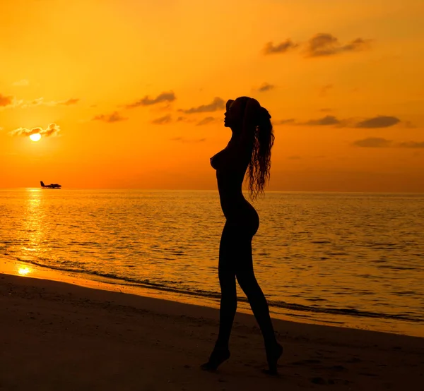 Sexy woman on sunset. Beautiful female model with perfect body is posing on sandy beach on Maldives Island. Sexy woman on a sunset background.