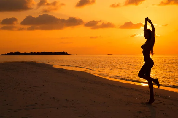 Sexy woman on sunset. Beautiful female model with perfect body is posing on sandy beach on Maldives Island. Sexy woman on a sunset background.