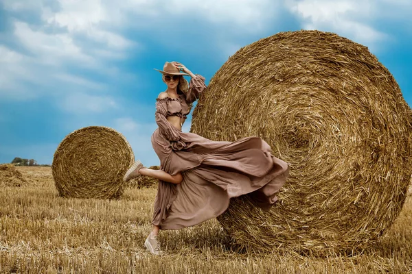 Beautiful female model in a fashionable dress and shoes is posing in a grain field on summer day. Sensual woman in country style posing against the countryside. Outdoor rural session. Rural girl.