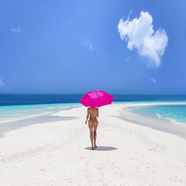Sexy bikini body woman on paradise tropical beach having fun on Maldives. Beautiful female model is holding pink umbrella and is walking on the sandy beach. Sexy girl in bikini on a paradise beach.