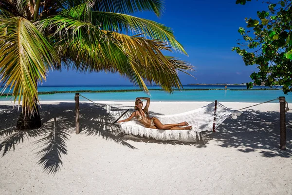 Beautiful sexy tanned woman in golden bikini on Maldives island. Young glamour girl is posing on hammock in paradise . Perfect body bikini model on Maldives beach. Bikini fashion. Luxury travel.