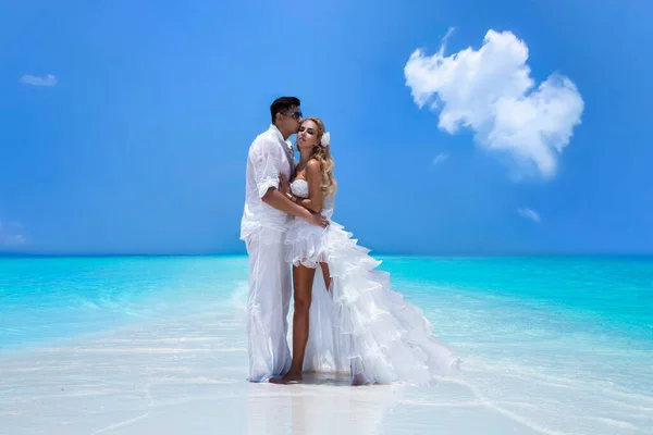 Summer love. Beautiful happy young couple in wedding clothes is standing on a beach in the Maldives. Engagements and wedding on the beach on the paradise island of Maldives. Luxury travel.