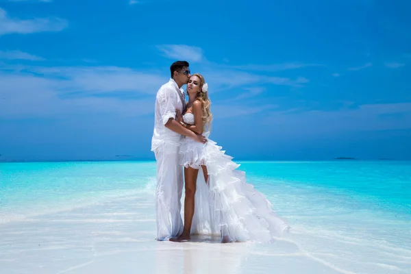 Summer love. Beautiful happy young couple in wedding clothes is standing on a beach in the Maldives. Engagements and wedding on the beach on the paradise island of Maldives. Luxury travel.