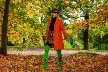 Güzel kadın sonbahar sahnesinde renkli yapraklı sonbahar kıyafetleri giyiyor. Açık hava çekimi. Sonbahar modası.