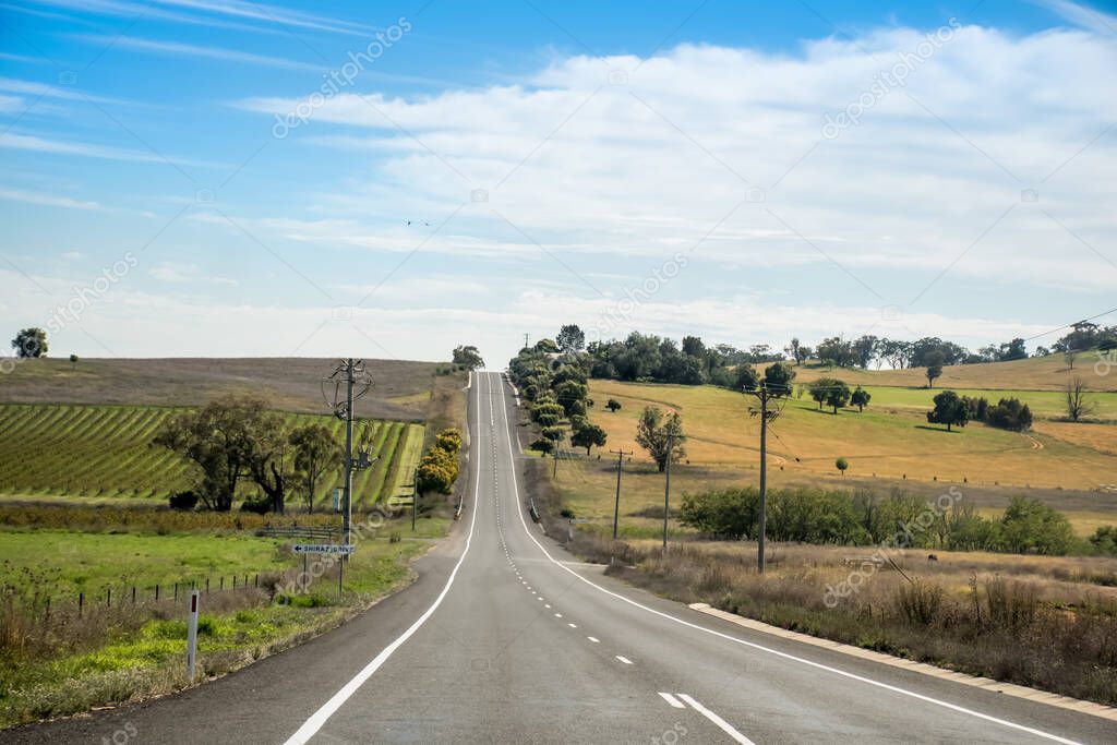 Straight open empty road surrounded by farms and fields near Nimmitabel in Australia. Road trip travel concept