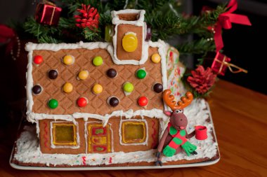 Krema, şeker, biblo, lolipop ve arkaplanda bulanık Noel ağacı olan şeker kamışlarıyla süslenmiş ev yapımı zencefilli kurabiye evi..