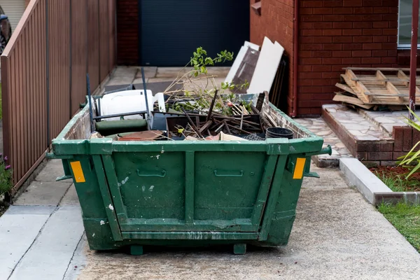 Skip bin with household waste rubbish on a front yard. House clean up renovation concept.