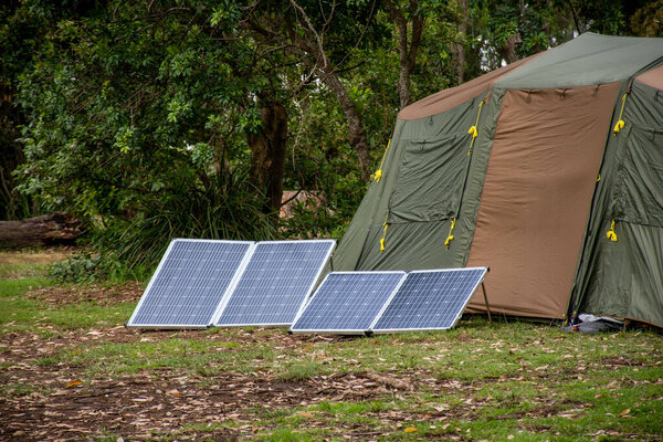 Portable foldable solar panels and Tent at the campsite surrounding by nature. Camping and recreation concept
