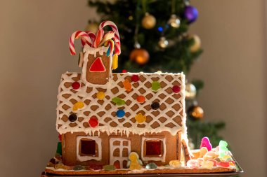 Krema, şeker, biblo, lolipop ve arkaplanda bulanık Noel ağacı olan şeker kamışlarıyla süslenmiş ev yapımı zencefilli kurabiye evi..