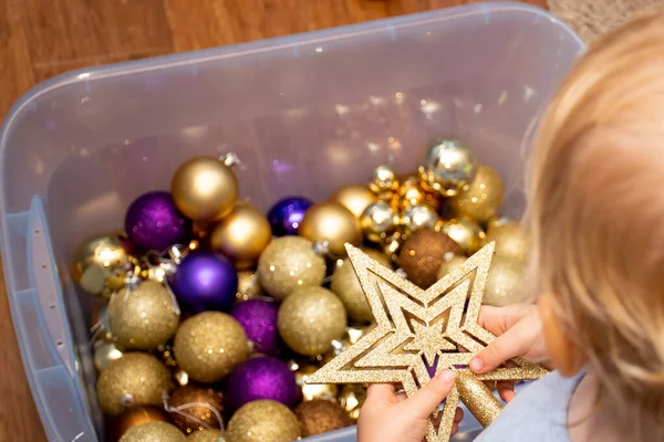 Elinde Noel süsleri olan küçük bir çocuk plastik bir kutuda Noel ağacını süslemeye hazır bekliyor. Noel süslemeleri deposu