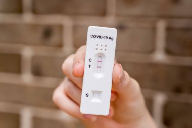 Covid-19 'un hızlı antijen test kasedini tutan eller evde yapılan hızlı tanı testi sonucu pozitif çıktı.