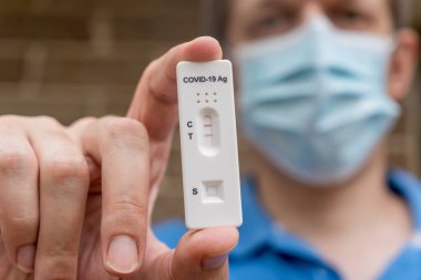 Covid-19 hızlı antijen test kasedini elinde tutan maskeli bir adam hızlı teşhis testinin negatif sonucunu taşıyor. Evde kendi kendini test etme kiti