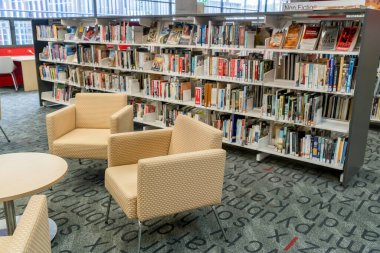 Sydney, Avustralya - 2022-01-25 Halk kütüphanesinde. Kitaplarla dolu kitap rafları ve okuyucular için sandalyeler. Cronulla Kütüphanesi, NSW.
