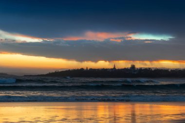 Okyanusun kumlu sahilinde gün batımının manzarası. Ufukta kasabanın silueti var. Manzara manzaralı seyahat arka planı. Kumdaki florptintler. Avusturalya