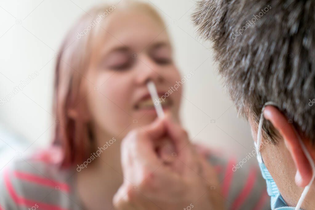 Selective focus bokeh shot of man wearing face mask and teenage girl while doing rapid antigen test nasal swab. Rapid diagnostic test kit usage