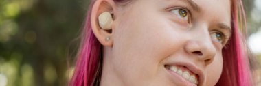 Elinde kablosuz kulaklık kulaklığı olan koyu pembe saçlı genç bir kız. Müzik telefon görüşmeleri podcast ses kayıtları dinleme konsepti