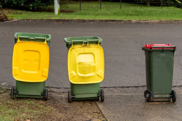 Australian garbage wheelie bins with colourful lids for recycling and general household waste lined up on the street kerbside for council rubbish collection