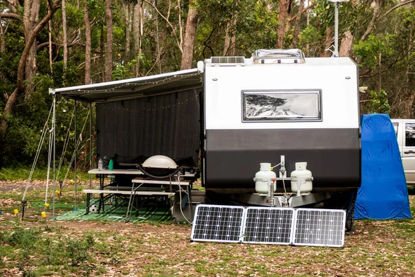 RV caravan camper on a campsite in the bush forest nature. Awning, portable toilet, solar panels, bbq, table. Family camping set up