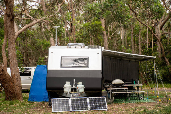 RV caravan camper on a campsite in the bush forest nature. Awning, portable toilet, solar panels, bbq, table. Family camping set up