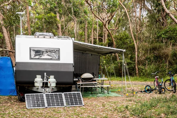 RV caravan camper on a campsite in the bush forest nature. Awning, portable toilet, solar panels, bbq, table. Family camping set up