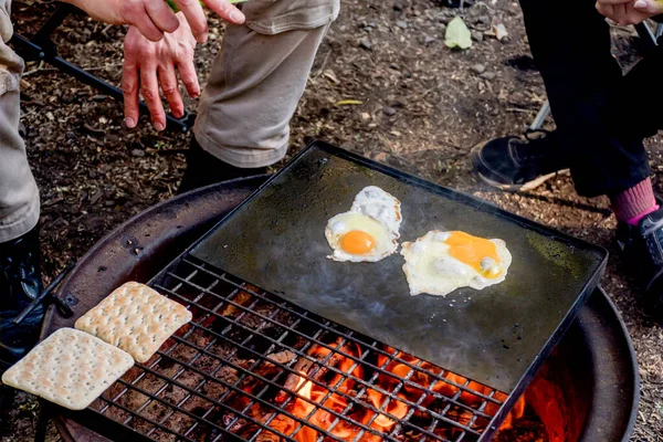 Breakfast camp cooking. Man cooking eggs and warming bread on a cast iron plate over the camp fire. Camping lifestyle