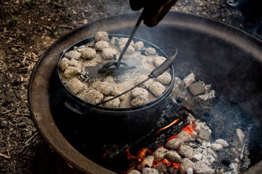 Dutch oven camp cooking with coal briquettes beads on top. Campfire in a firepit. Camping lifestyle