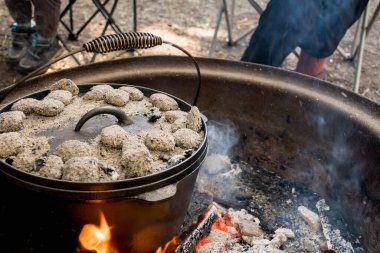 Dutch oven camp cooking with coal briquettes beads on top. Campfire in a firepit. Camping lifestyle
