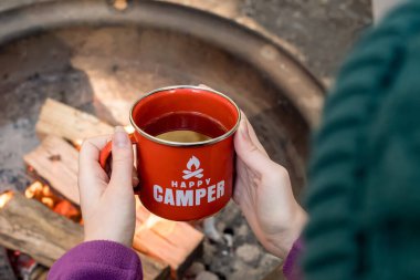 Kamp yaşam tarzı. Kamp ateşinin yanında elinde kırmızı diş minesi bardağı tutan bereli bir kız. Mutlu kampçı.