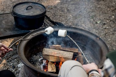 İnsanlar kamp ateşinin üzerinde büyük bir çubuk üzerinde büyük marşmelov kızartıyorlar. Aile eğlencesi.