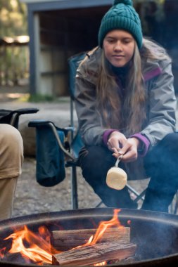 Bereli şapka takan genç bir kız kamp ateşinin üzerinde çubuk üzerinde büyük bir marşmelov pişiriyor. Kampçı aile eğlence yaşam tarzı