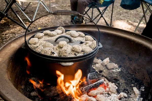 Dutch oven camp cooking with coal briquettes beads on top. Campfire in a firepit. Camping lifestyle