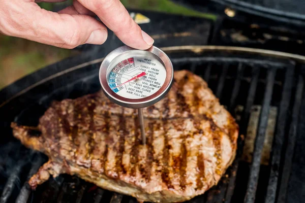 Beef blade steak grilling on barbecue grill plate with meat thermometer. Backyard BBQ grill cooking meat.