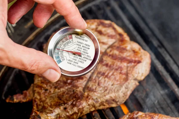 Beef blade steak grilling on barbecue grill plate with meat thermometer. Backyard BBQ grill cooking meat.