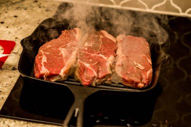 Grilling cooking new york beef strip sirloin steaks on cast iron grill pan skillet on a electric ceramic stove counter top at home