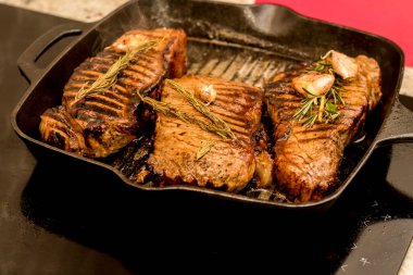 Grilling cooking New York beef sirloin strip steaks with rosemary and garlic on cast iron grill pan skillet on a ceramic stove counter top at home.