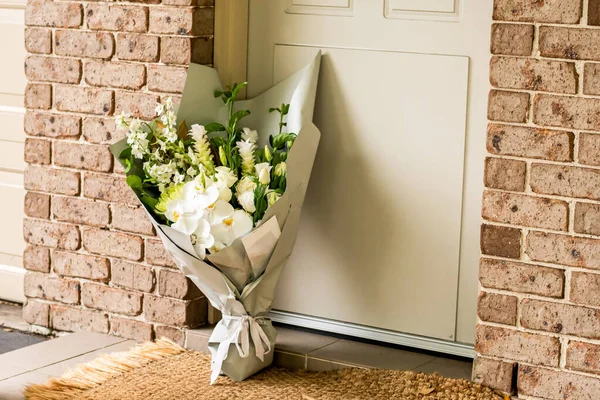 A bouquet of flowers delivered on a porch doorsteps of a house front door. Surprise contactless delivery. Mother\'s Day, Valentine\'s Day, Birthday, Anniversary and Celebration