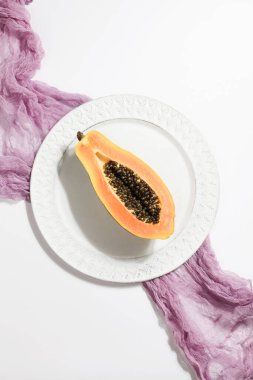 Beyaz arka planda mor tekstil olan tabakta papaya olan yaratıcı yiyecek konsepti. Düz manzaralı. Minimalist renkli doğa arkaplanı.