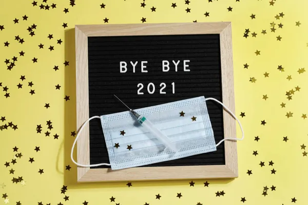 Tablero de letras negro con texto BYE BYE 2021 con pequeñas estrellas, jeringa y máscara sobre fondo amarillo. — Foto de Stock