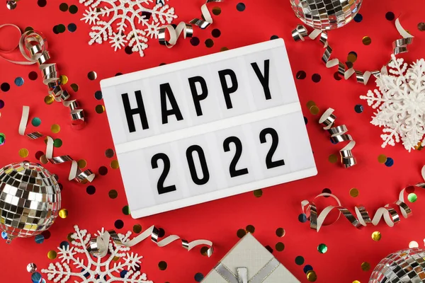 2022年の幸せな言葉のライトボックスギフトボックスと赤い背景の休日のコンフェッティ。新年のお祝いを. ストック写真