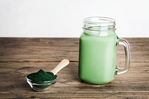Cam şişede taze yeşil smoothie ve ahşap arka planda kaşıkla spirulina tozu. kullanışlı alışkanlıklar — Stok fotoğraf