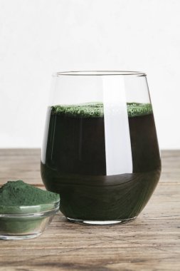 Taze yeşil içecek, camda spirulina, ahşap zemin üzerinde kaşık olan spirulina tozu. Yararlı alışkanlıklar, kişisel bakım ve sağlıklı yaşam tarzı. Kopya alanı
