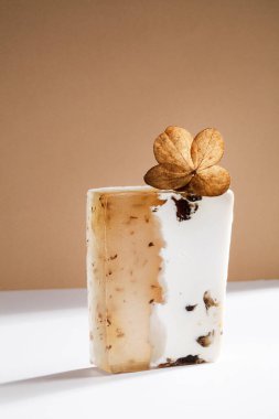 Beyaz ve kahverengi arka planda kuru yapraklı güzel el yapımı doğal sabun.