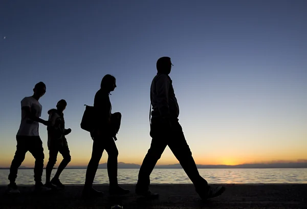 Silouetes de pessoas que caminham no pôr do sol — Fotografia de Stock
