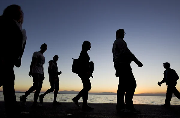 Silouetes de pessoas que caminham no pôr do sol — Fotografia de Stock